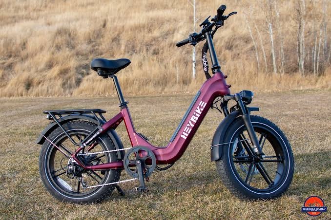 Maroon fat-tire step-through electric bike with front suspension and cargo rack, ideal for both urban streets and light off-road adventures.