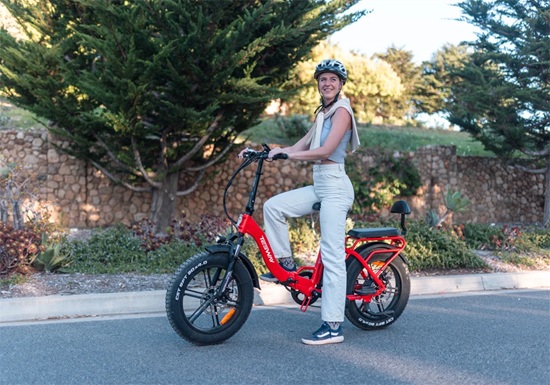 Senior-friendly red fat-tire e-bike being ridden outdoors, featuring a low-step frame, wide tires, and a comfortable upright riding position.
