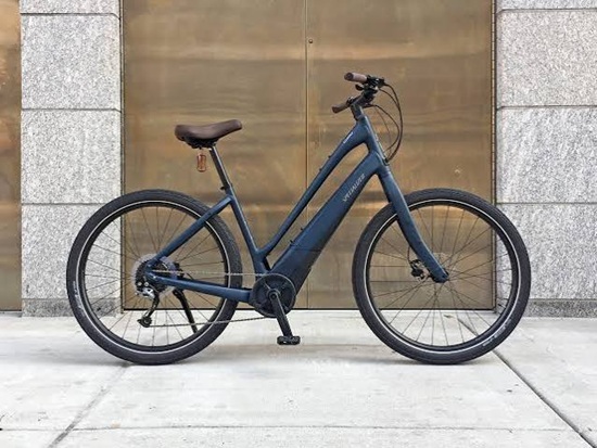 Navy blue step-through electric bicycle parked against a stone and gold wall.